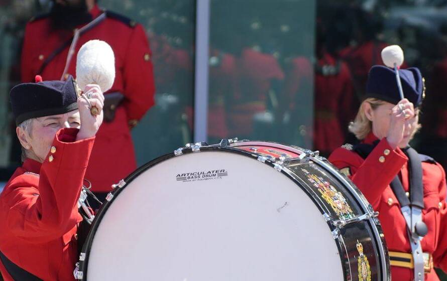 RCMP ceremonial band members in red serge uniforms playing drums during a public ceremony in Canada