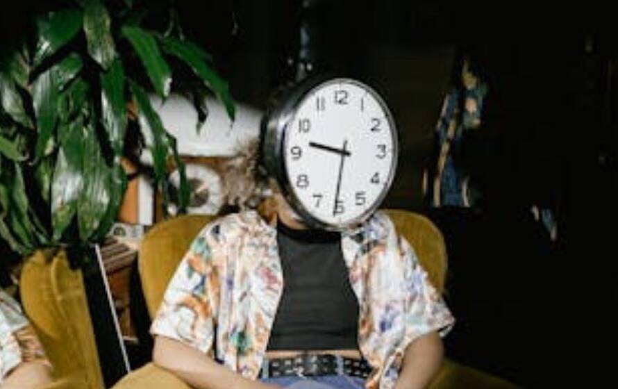 Person sitting indoors with a clock covering their face, symbolizing long RCMP application wait times, processing delays, and uncertainty during recruitment stages.