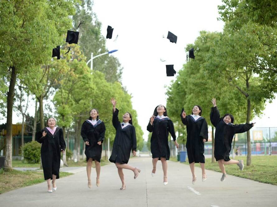 Graduates celebrating by tossing caps in the air on a bright day.