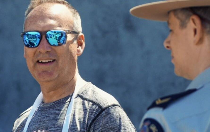 An RCMP officer in uniform and campaign hat speaks with a civilian man wearing reflective sunglasses during an outdoor public event in daylight.