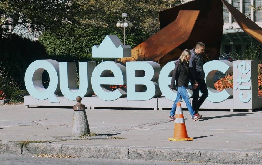 Large "Québec" city sign displayed in a public square with pedestrians walking nearby, representing the province of Quebec, provincial regulations, public services, and firearms licensing requirements.