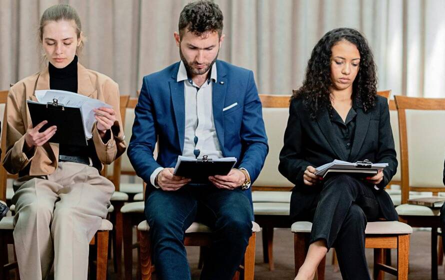 Group of professionally dressed job applicants seated in a waiting area reviewing documents and clipboards before interviews, representing RCMP recruitment and hiring opportunities in Regina, Saskatchewan.