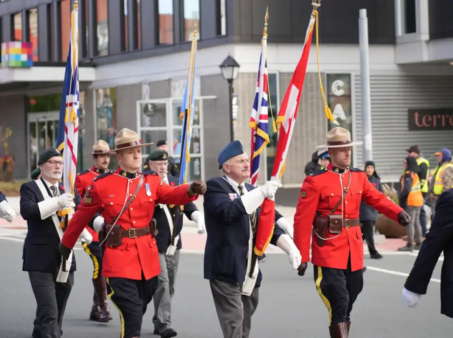 RCMP officers and veterans march with Canadian and provincial flags during a Remembrance Day parade in a Canadian downtown