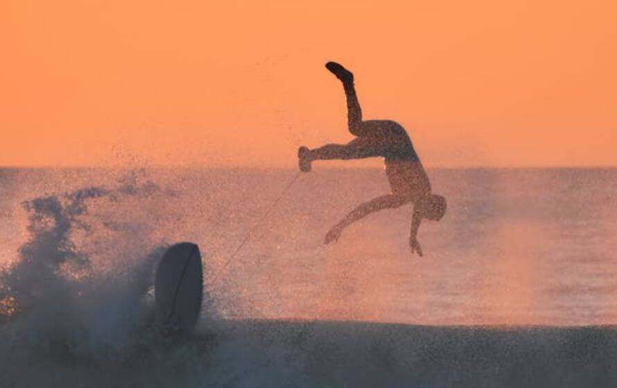 Person performing an acrobatic flip into ocean waves at sunset, symbolizing risk, uncertainty, and major life transitions during the RCMP application process.